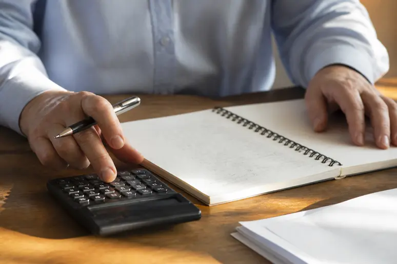 Mains d'une personne calculant un budget mensuel avec une calculatrice et un stylo sur un bureau.