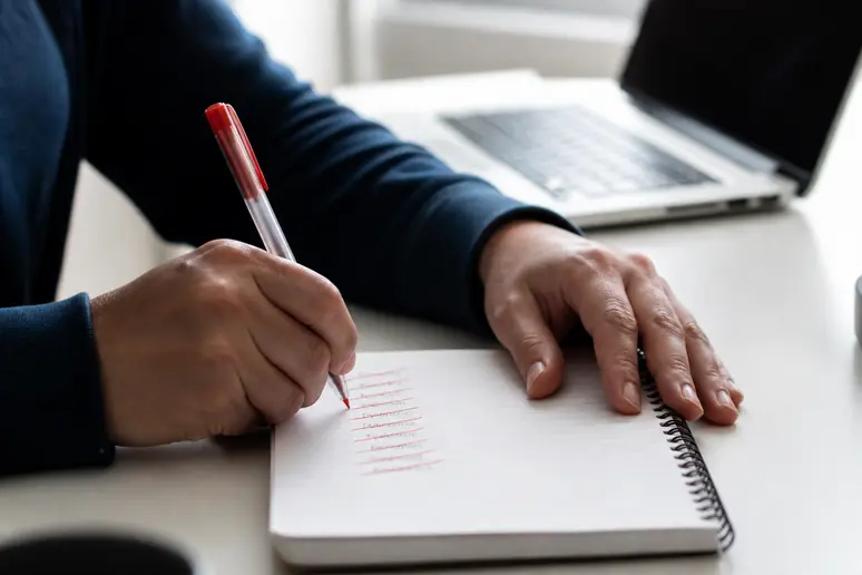 Mains écrivant des mots-clés à exclure sur un carnet pour mieux cibler les annonces.