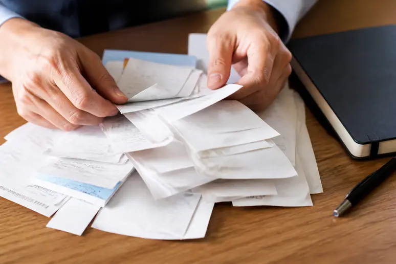 Mains triant des reçus de dépenses et des justificatifs sur un bureau en bois pour structurer un tableau