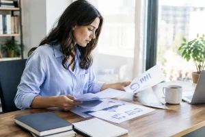Un professionnel analyse des rapports papier avec un logiciel de newsletter dans un bureau lumineux.